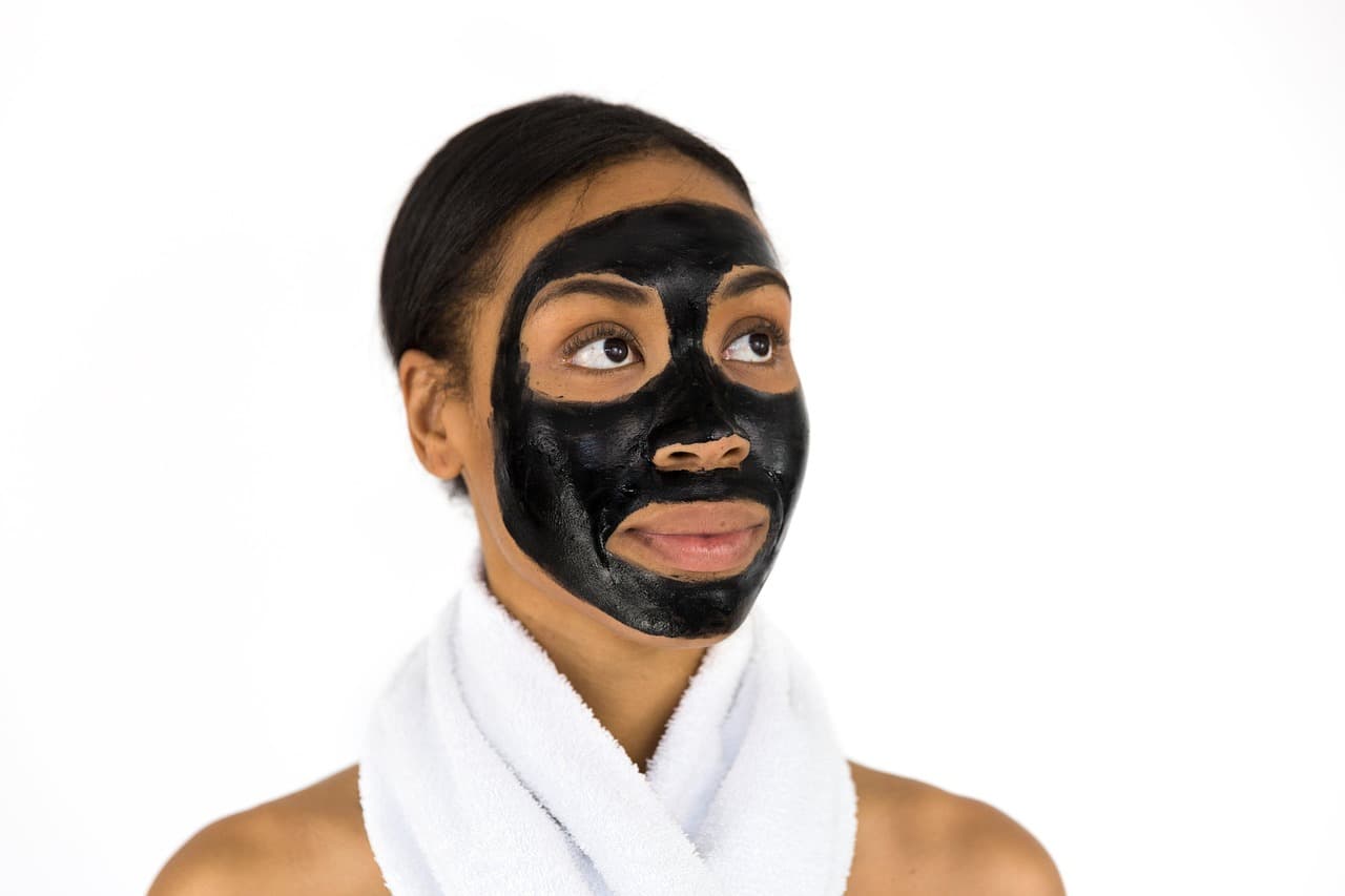 Woman in a charcoal face mask with a white towel round her shoulders