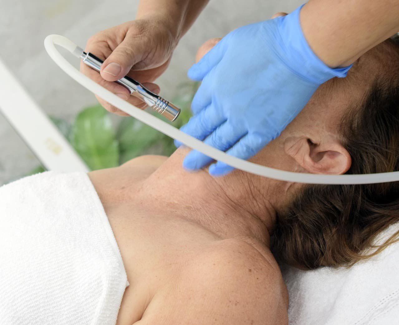 Gloved hands guiding a treatment handpiece along a client's neck